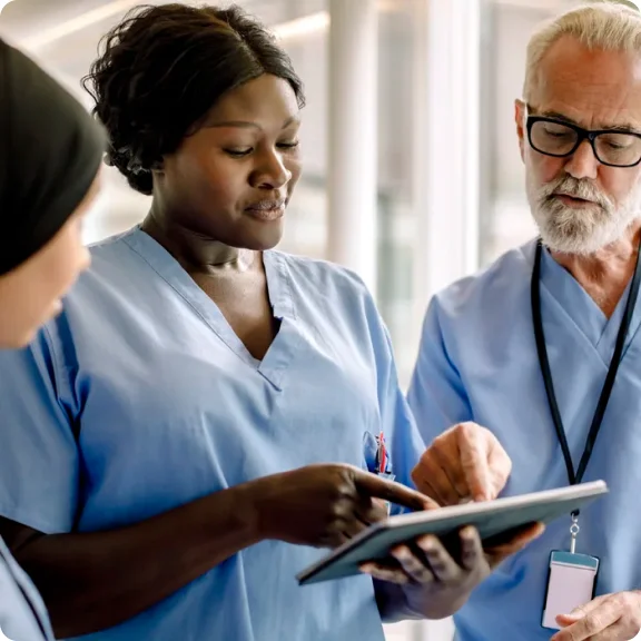 Drie zorgprofessionals kijken naar een tablet en bespreken deze.